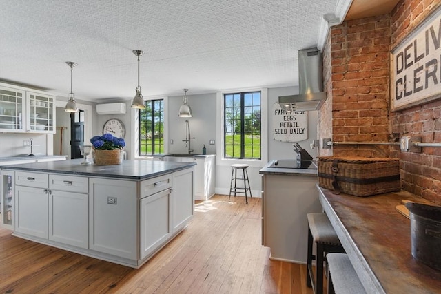 4 Porter St, Granby, MA 01033 - kitchen with dark countertops, an AC wall unit, brick wall, white cabinetry, and light wood-type flooring