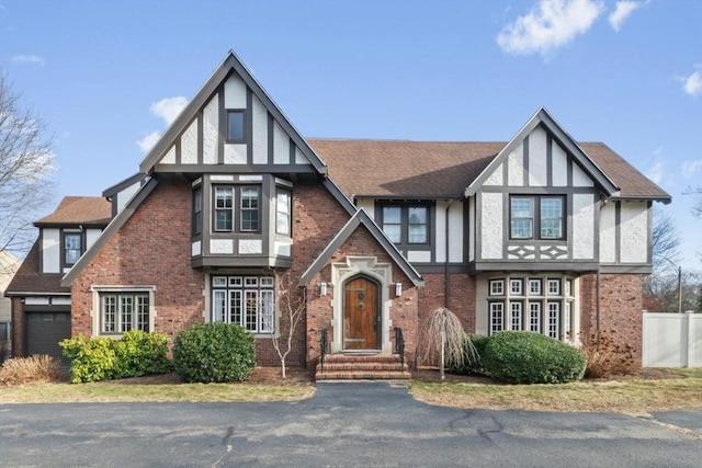 tudor-style house with an attached garage, stucco siding, roof with shingles, and brick siding