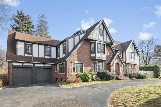 english style home featuring an attached garage, stucco siding, aphalt driveway, and brick siding