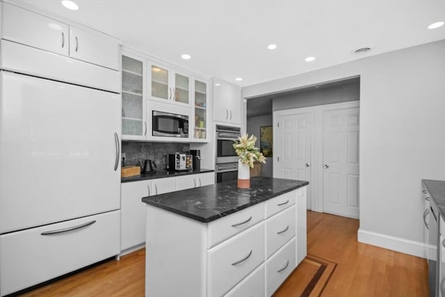 kitchen featuring dark countertops, glass insert cabinets, white cabinets, and built in appliances