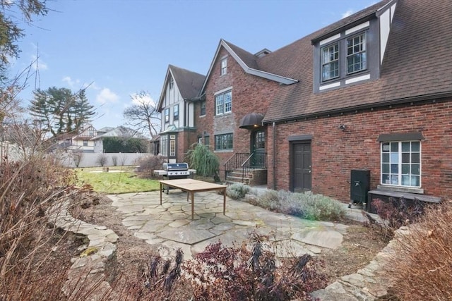 view of property exterior featuring brick siding, roof with shingles, a patio area, and fence