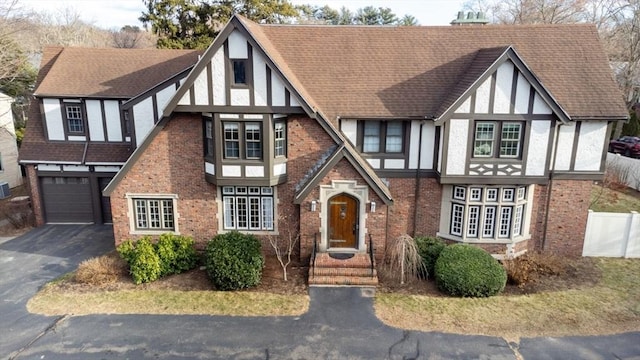 tudor-style house with brick siding, a shingled roof, aphalt driveway, and stucco siding