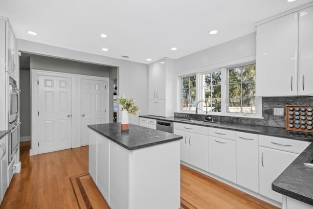 kitchen with a center island, light wood finished floors, backsplash, white cabinetry, and a sink