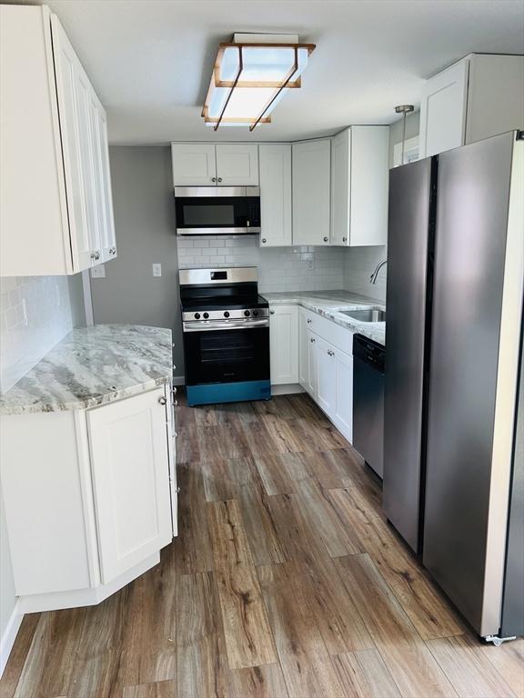 209 Casey Dr, Chicopee, MA 01020 - kitchen with stainless steel appliances, dark wood-type flooring, backsplash, light stone countertops, and white cabinetry
