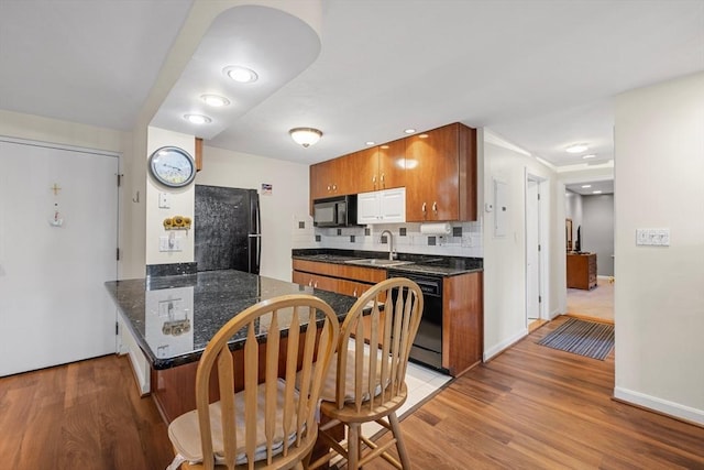 kitchen featuring light wood-style flooring, a peninsula, black appliances, and dark countertops