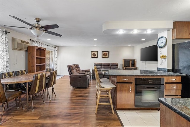 kitchen with brown cabinets, ceiling fan, light wood-style floors, a wall mounted AC, and black appliances
