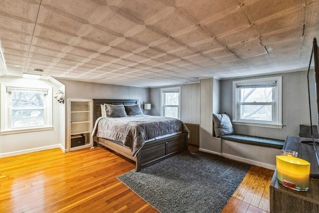 bedroom with wood-type flooring, radiator, and multiple windows