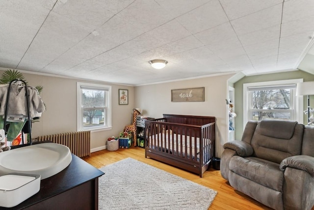 bedroom with multiple windows, radiator heating unit, and light hardwood / wood-style floors