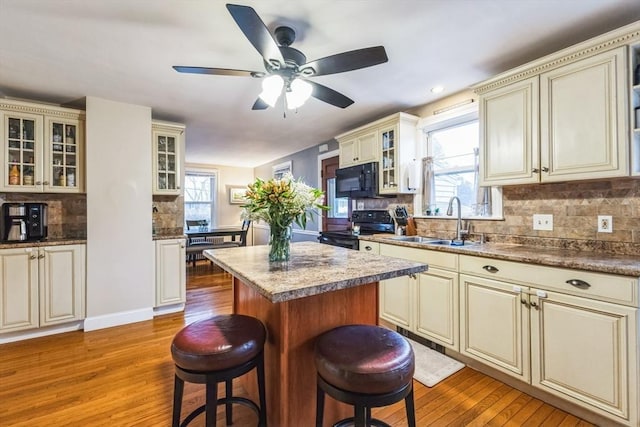 kitchen featuring cream cabinetry, light hardwood / wood-style flooring, a kitchen island, and black appliances