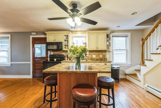 kitchen featuring a baseboard heating unit, light stone counters, cream cabinets, black appliances, and a kitchen island