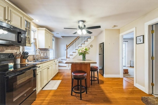 kitchen featuring a kitchen island, a kitchen breakfast bar, black appliances, cream cabinets, and light hardwood / wood-style flooring