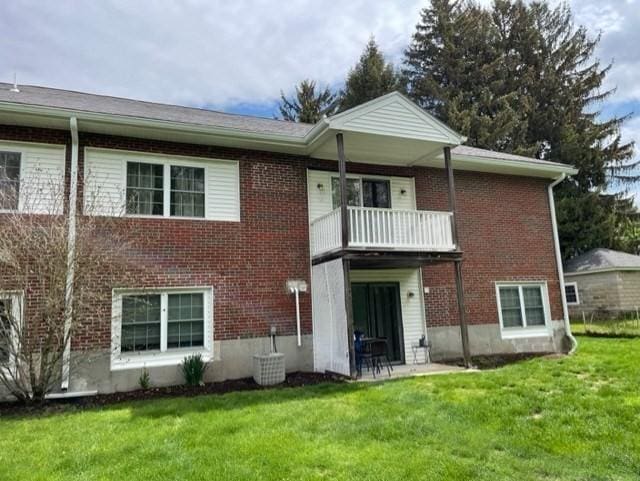 rear view of property with a balcony, a lawn, brick siding, and a patio