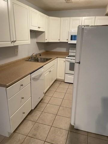 kitchen with white appliances, a sink, light tile patterned floors, and white cabinetry