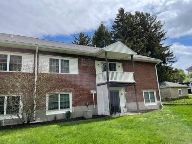 back of property with a balcony, a yard, brick siding, and central AC unit