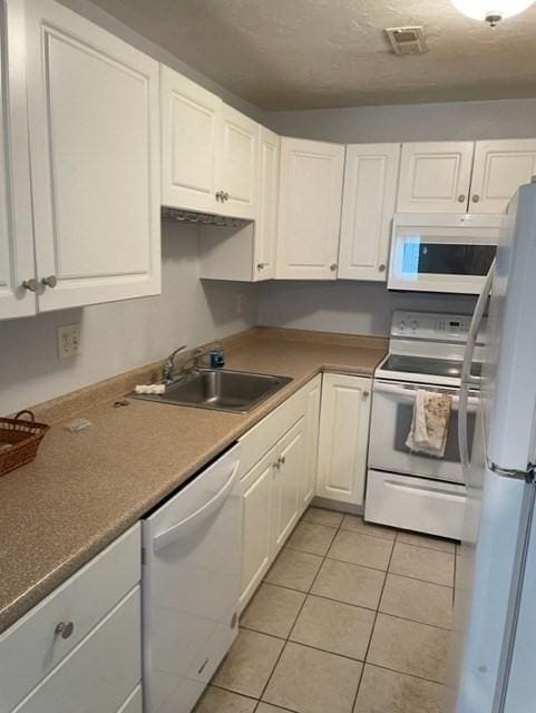 kitchen with white appliances, a sink, white cabinets, and light tile patterned floors