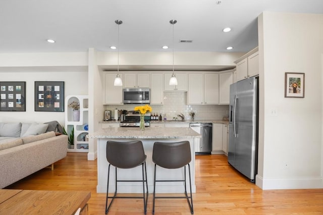129 Highland Ave Unit 4, Somerville, MA 02143 - kitchen featuring appliances with stainless steel finishes, a kitchen bar, tasteful backsplash, light stone counters, and light wood finished floors
