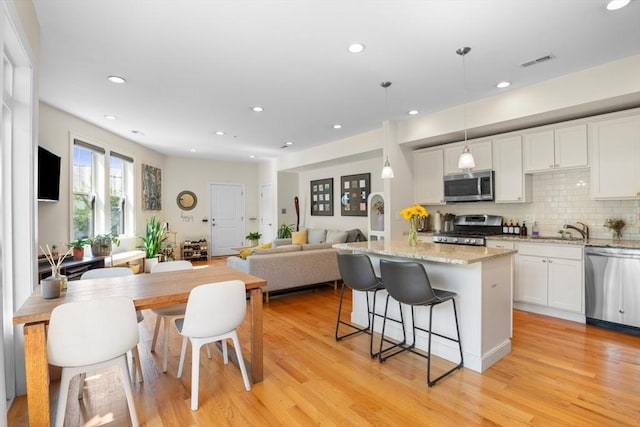 129 Highland Ave Unit 4, Somerville, MA 02143 - kitchen with stainless steel appliances, a center island, white cabinetry, a breakfast bar, and light wood-style floors
