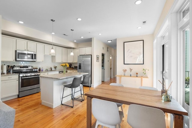 129 Highland Ave Unit 4, Somerville, MA 02143 - kitchen featuring appliances with stainless steel finishes, a center island, light wood finished floors, decorative backsplash, and recessed lighting