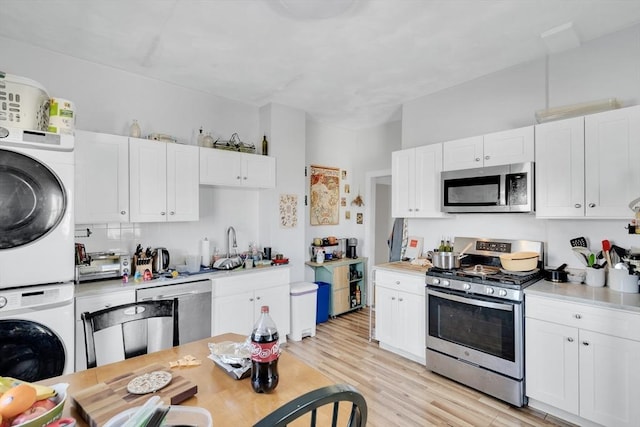 kitchen featuring stainless steel appliances, stacked washer / dryer, white cabinetry, and light hardwood / wood-style flooring