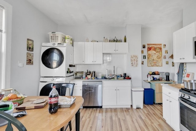 kitchen with sink, white cabinets, stacked washer / drying machine, light hardwood / wood-style floors, and stainless steel appliances