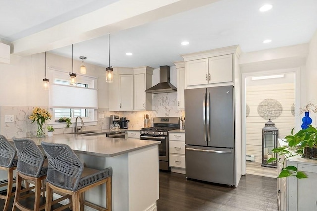 kitchen with appliances with stainless steel finishes, a sink, a peninsula, wall chimney exhaust hood, and dark wood-type flooring