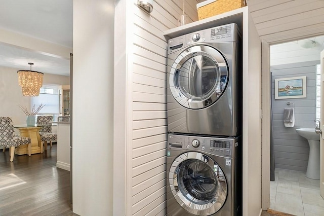 clothes washing area with wooden walls, laundry area, a chandelier, and stacked washer and clothes dryer
