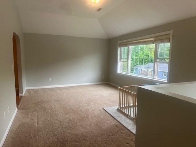 carpeted spare room with lofted ceiling, baseboards, and arched walkways