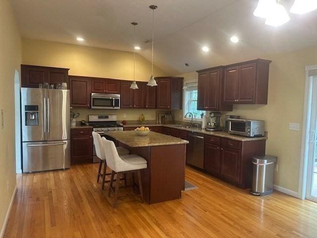 kitchen with stainless steel appliances, light wood-style floors, a sink, vaulted ceiling, and a kitchen island