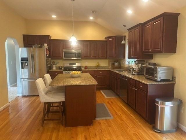 kitchen with appliances with stainless steel finishes, light stone counters, a center island, lofted ceiling, and light wood-type flooring
