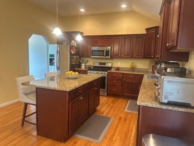 kitchen with stainless steel appliances, lofted ceiling, a breakfast bar area, light wood-style flooring, and hanging light fixtures