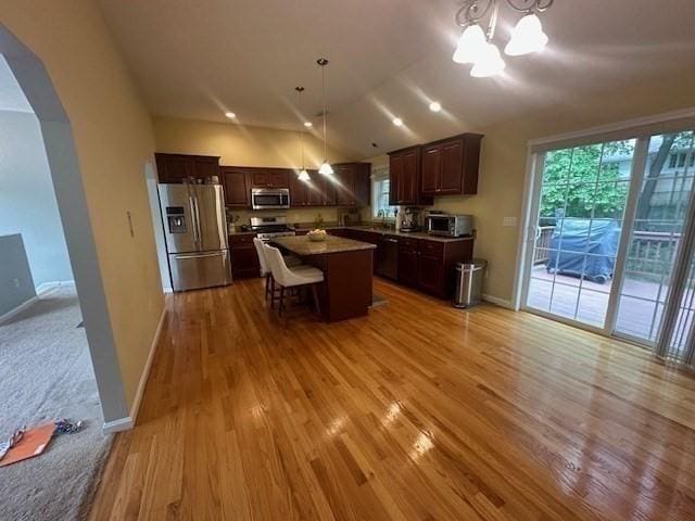 kitchen featuring appliances with stainless steel finishes, arched walkways, light wood finished floors, a chandelier, and vaulted ceiling