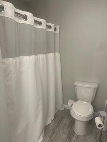 bathroom featuring wood finished floors, toilet, baseboards, and curtained shower