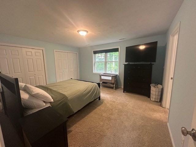 bedroom with two closets, light carpet, and baseboards