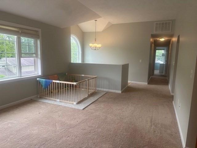 carpeted spare room with a chandelier, vaulted ceiling, and baseboards
