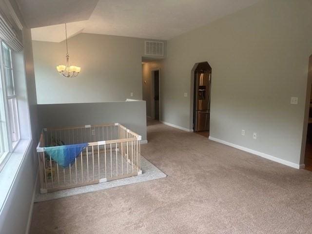 spare room with carpet flooring, a chandelier, lofted ceiling, arched walkways, and baseboards