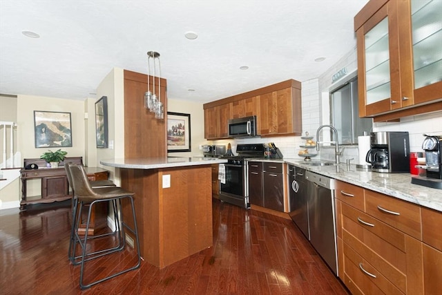 kitchen featuring stainless steel appliances, a sink, dark wood-style floors, brown cabinets, and glass insert cabinets