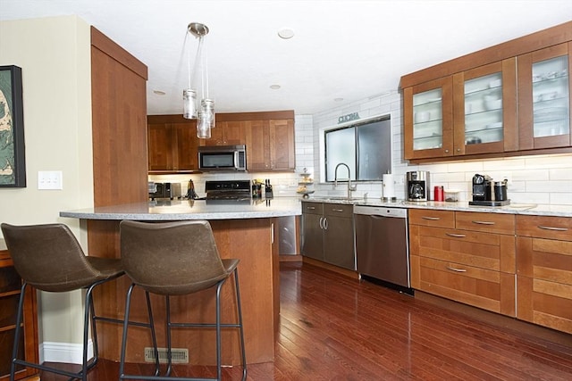 kitchen with appliances with stainless steel finishes, a kitchen bar, decorative backsplash, and glass insert cabinets