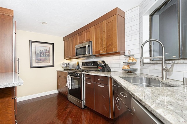 kitchen with appliances with stainless steel finishes, a sink, baseboards, dark wood finished floors, and light stone counters