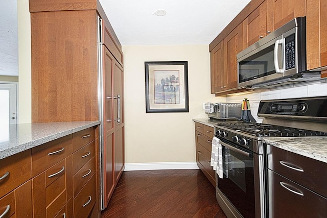 kitchen with appliances with stainless steel finishes, dark wood finished floors, baseboards, and light stone counters