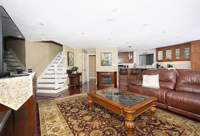 living area featuring dark wood-style flooring, stairs, baseboards, recessed lighting, and a glass covered fireplace