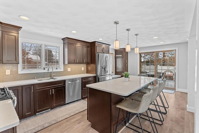 kitchen featuring appliances with stainless steel finishes, a kitchen island, decorative light fixtures, light hardwood / wood-style floors, and sink