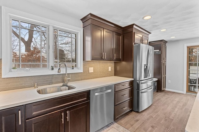 kitchen featuring appliances with stainless steel finishes, tasteful backsplash, sink, light wood-type flooring, and dark brown cabinets