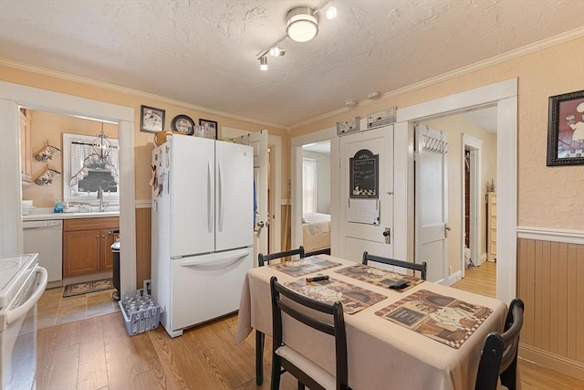 dining area featuring light wood-style flooring, wainscoting, ornamental molding, and a textured ceiling