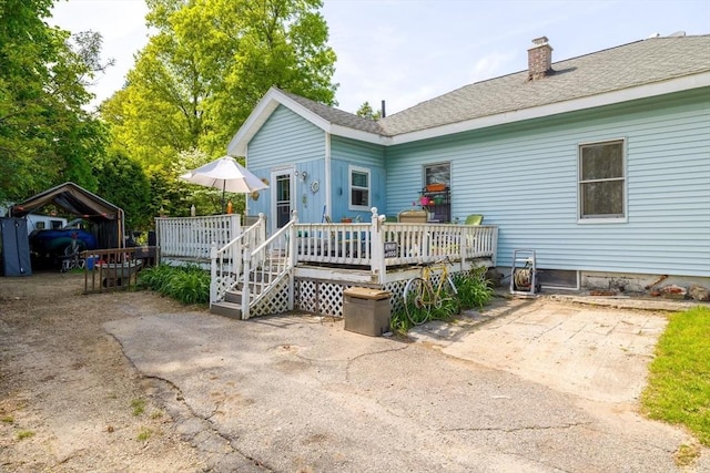 back of house featuring a deck, a chimney, and a shingled roof