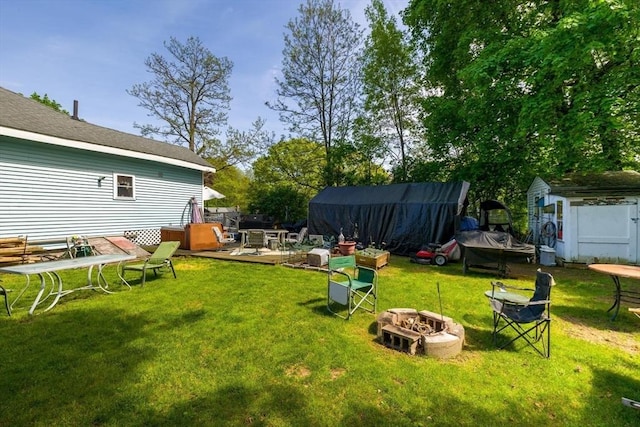 view of grassy yard featuring a fire pit, a storage unit, an outbuilding, and a deck