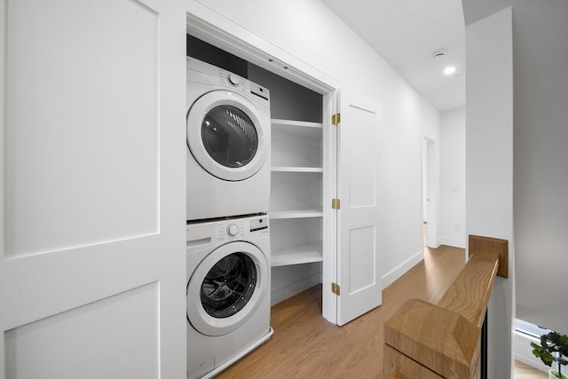 laundry area with stacked washer / dryer, wood finished floors, and baseboards