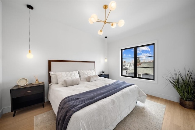 bedroom with a chandelier, light wood-type flooring, and baseboards