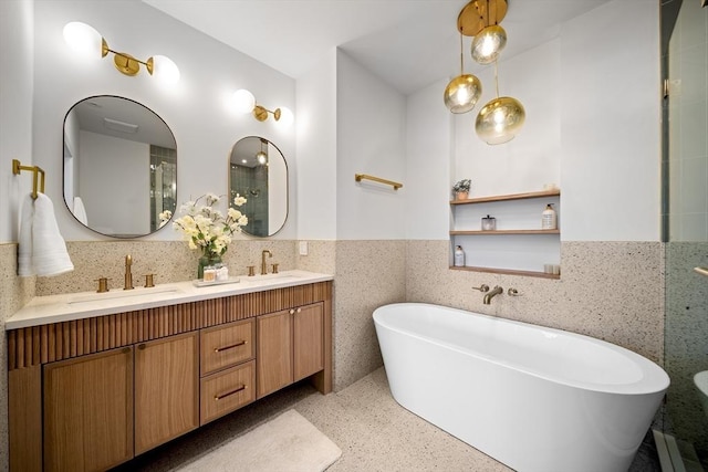 bathroom with speckle patterned floor, tile walls, a wainscoted wall, double vanity, and a freestanding tub