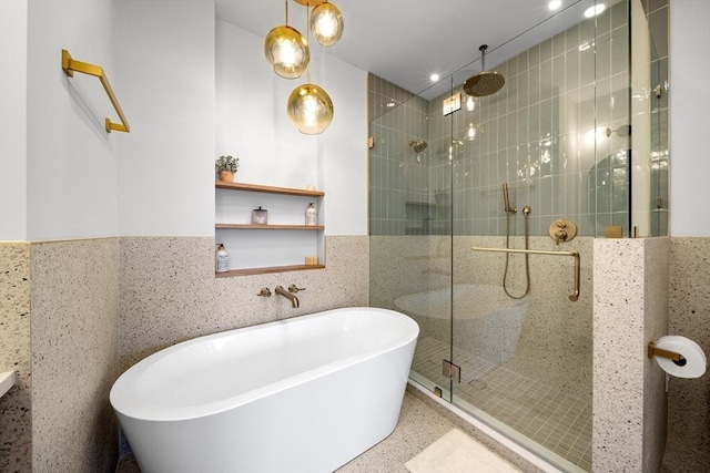 bathroom with a shower stall, speckle patterned floor, a freestanding tub, tile walls, and a wainscoted wall