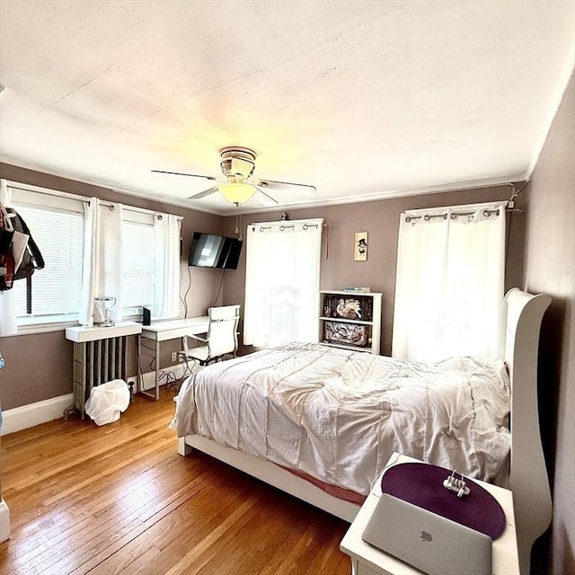 bedroom featuring wood-type flooring, baseboards, a ceiling fan, and radiator heating unit